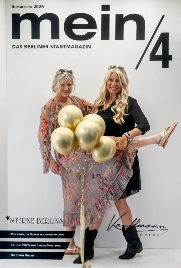 Vor einer Fotowand mit der Aufschrift „mein/4