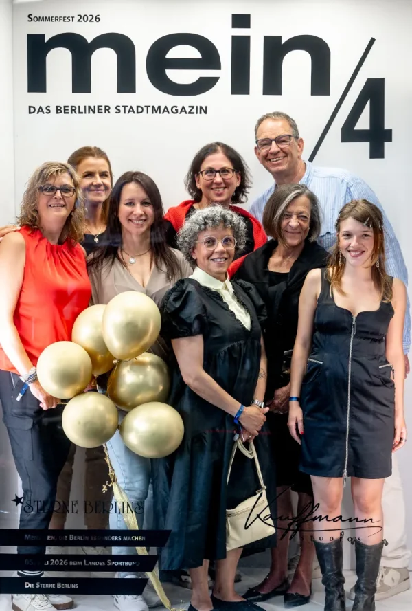 Vor einer Fotowand mit der Aufschrift „mein/4