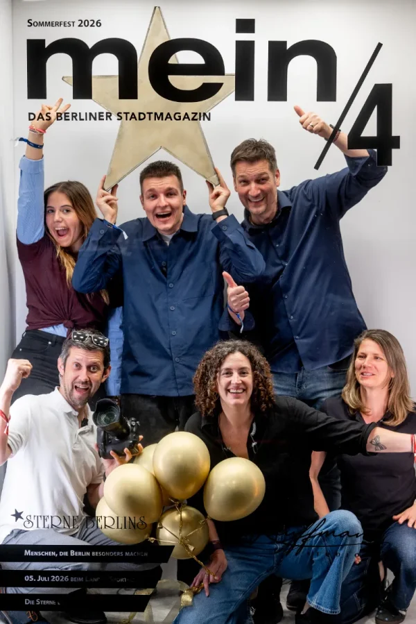 Vor einer Fotowand mit der Aufschrift „mein/4