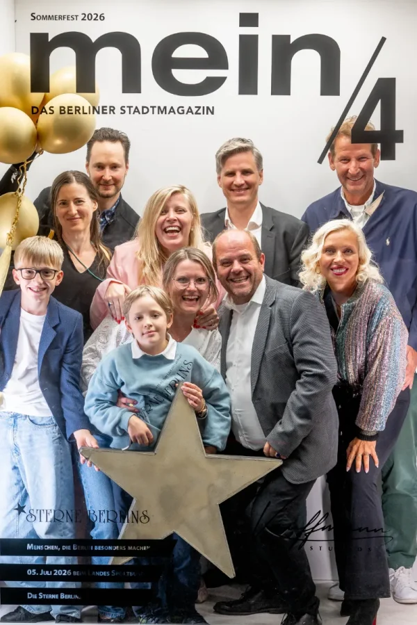 Vor einer Fotowand mit der Aufschrift „mein/4