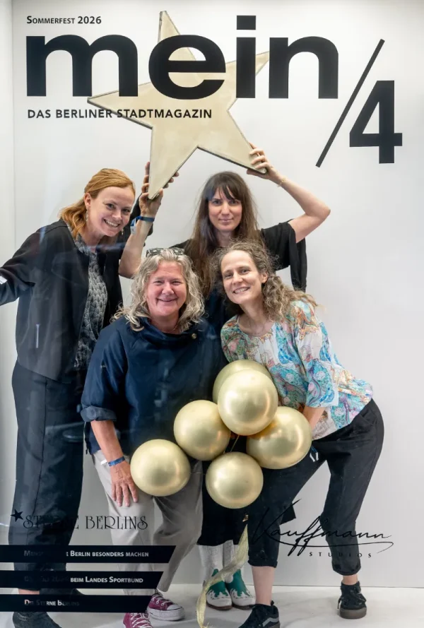 Vor einer Fotowand mit der Aufschrift „mein/4