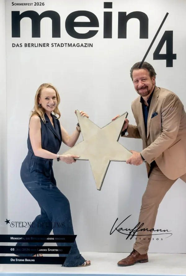Vor einer Fotowand mit der Aufschrift „mein/4