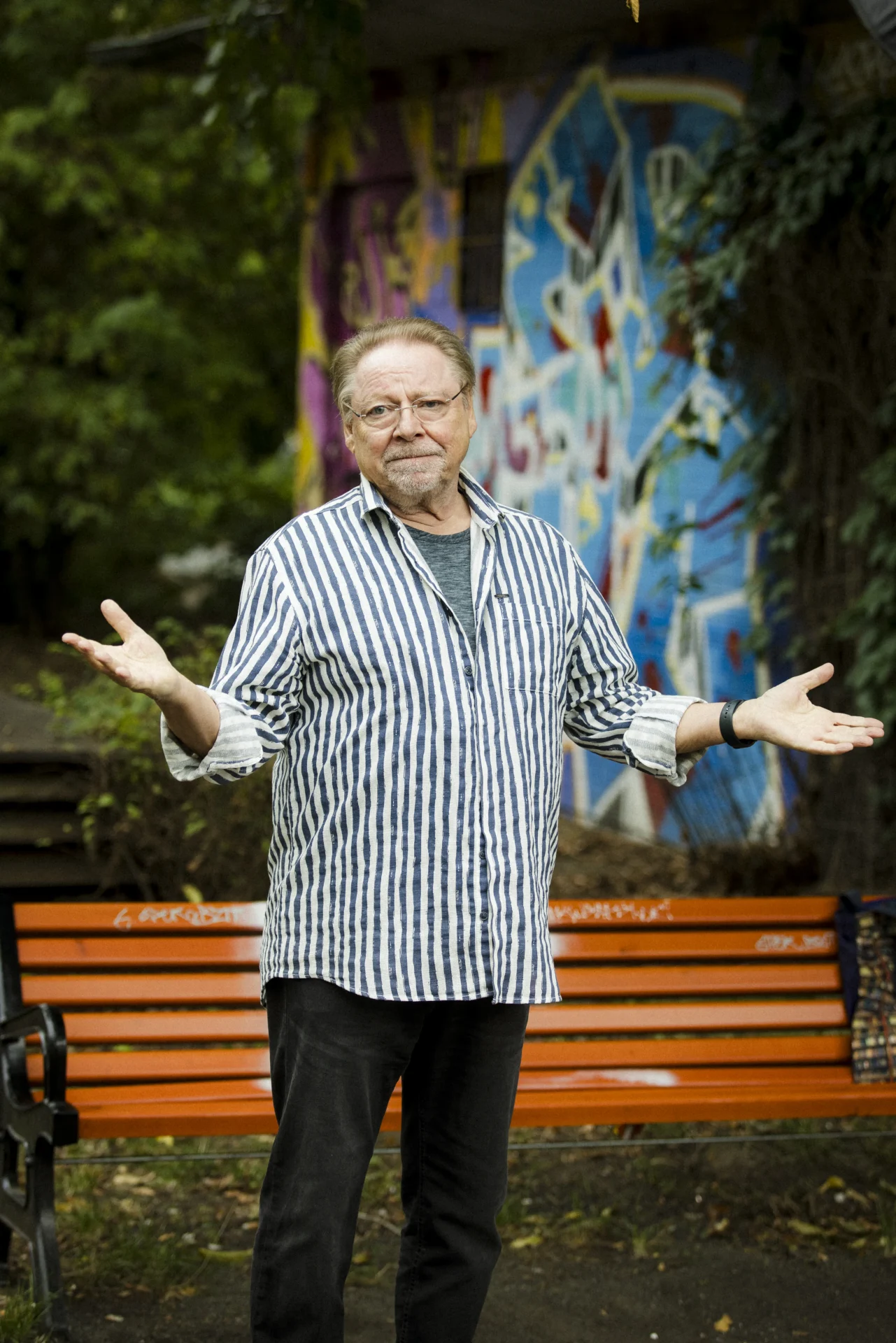 Jürgen von der Lippe steht in gestreiftem Hemd vor einer bunten Graffiti-Wand