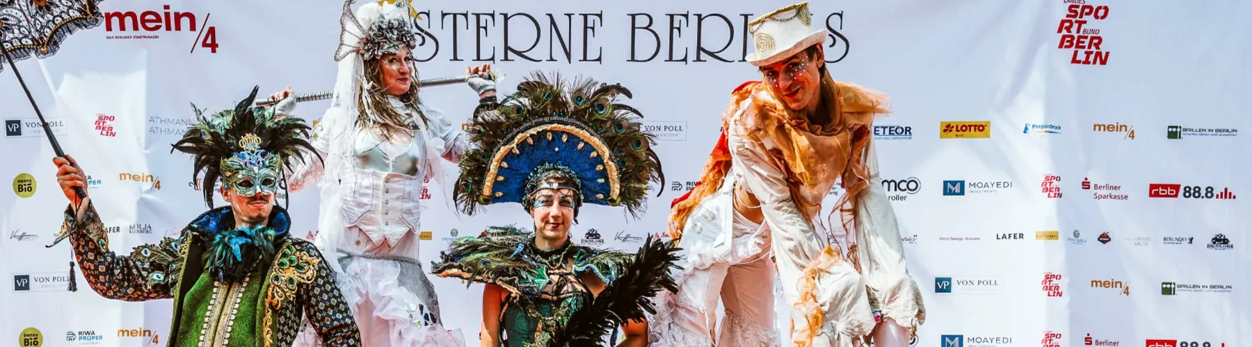 4 verkleidete Performancekünstler vor Plakatwand