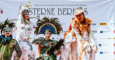 4 verkleidete Performancekünstler vor Plakatwand