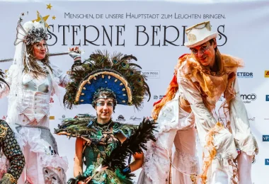 4 verkleidete Performancekünstler vor Plakatwand