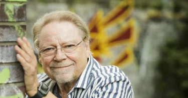 Jürgen von der Lippe lehnt lächelnd an einer Ziegelmauer