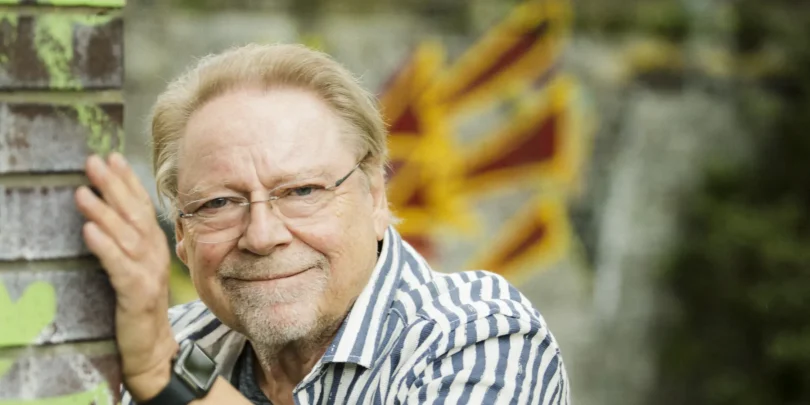 Jürgen von der Lippe lehnt lächelnd an einer Ziegelmauer